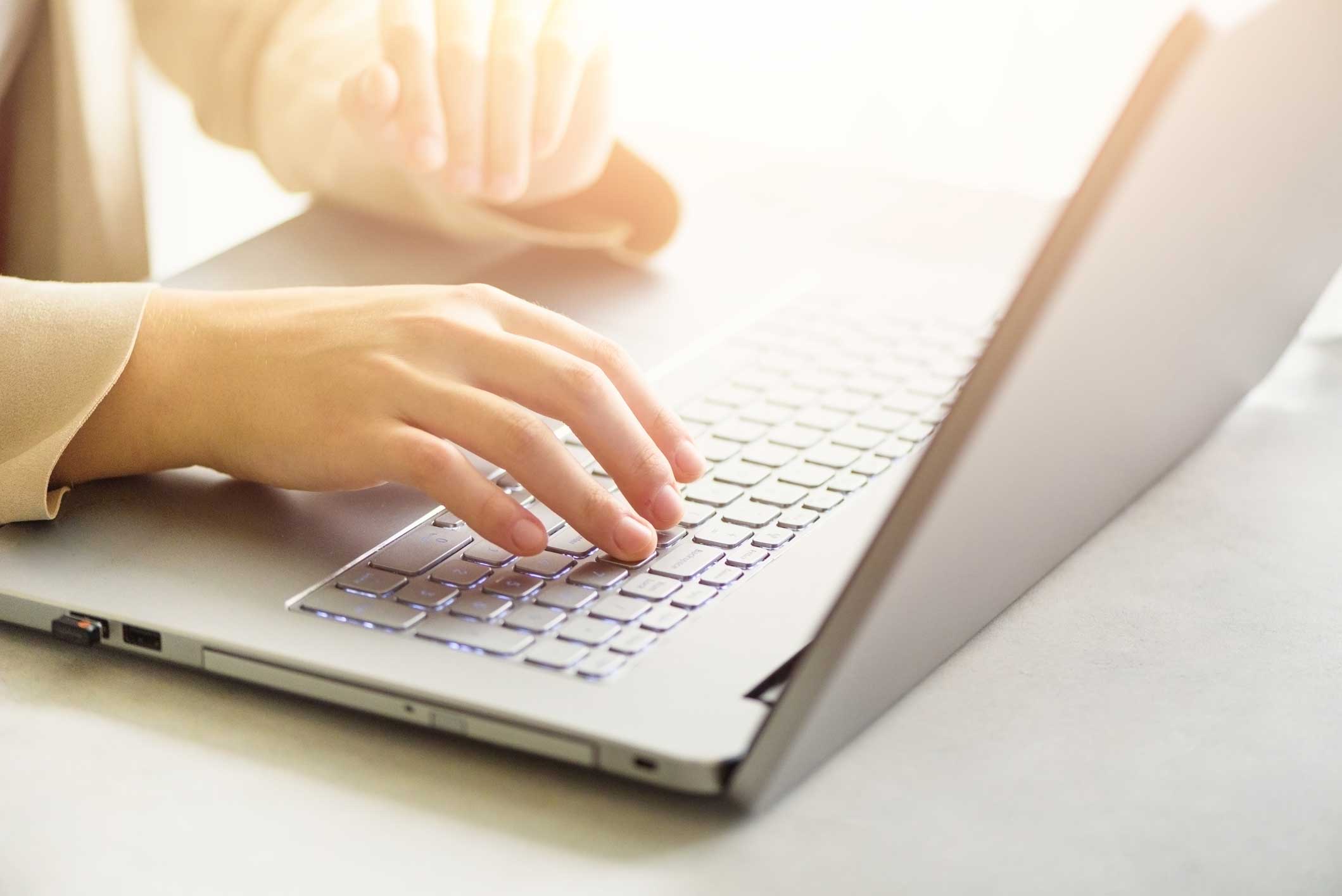 Woman working on computer close up. Woman hands typing on keyboard of laptop, online shopping detail. Business, remote work, always connect, online banking concept. Sunlight bokeh effect.